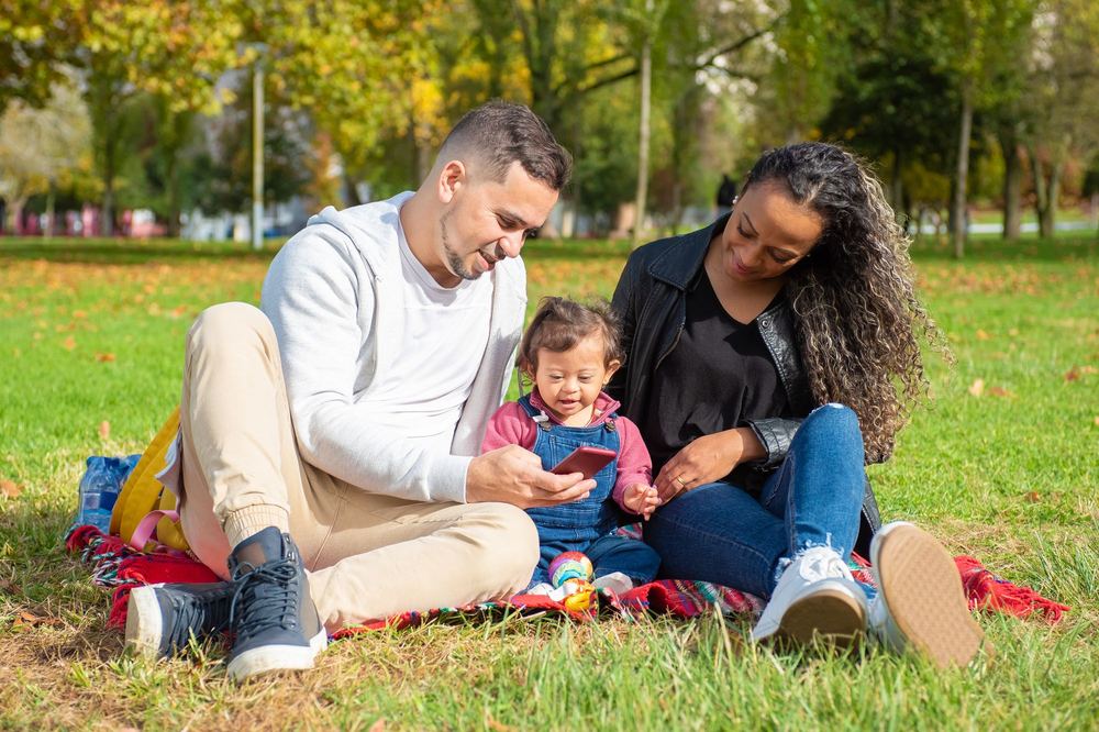 Parents sitting on a picnic blanket in a park with their young child