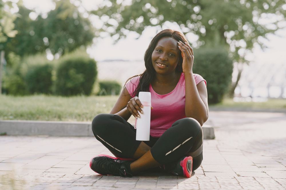 Woman in activewear resting outdoors with a water bottle, smiling